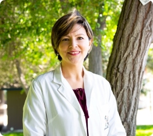A woman in a lab coat standing in front of a tree.